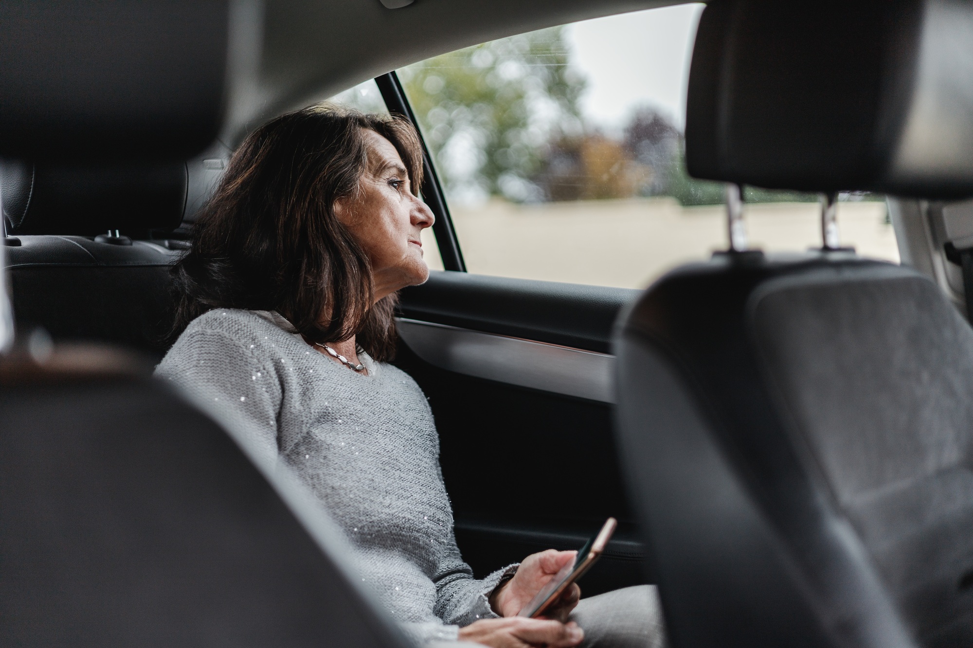 latinx mature woman waiting inside a taxi and looking through the window